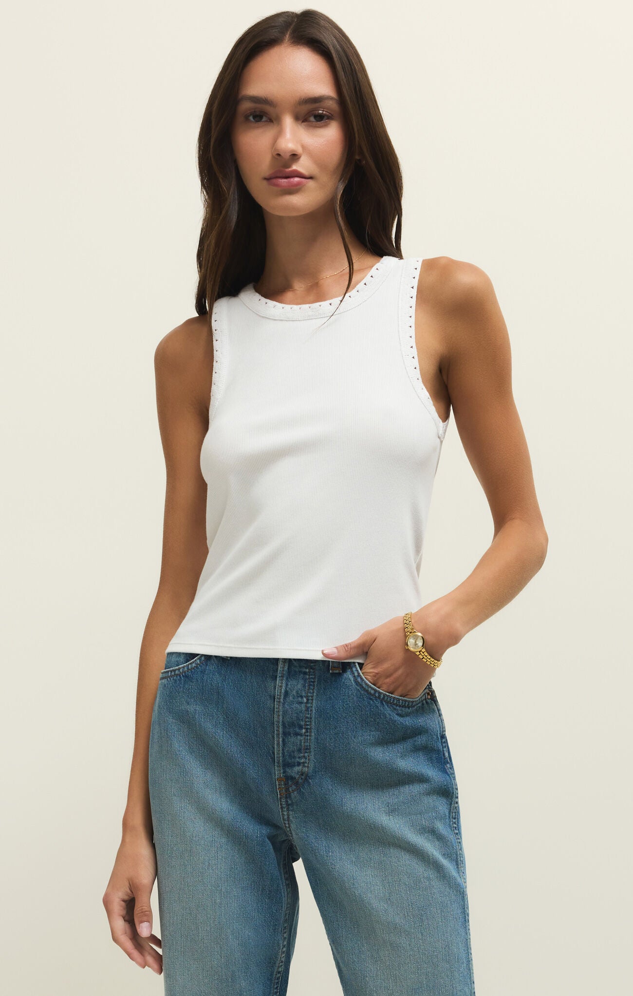 Woman wearing a white tank top and blue jeans against a plain background