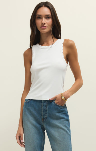 Woman wearing a white tank top and blue jeans against a plain background