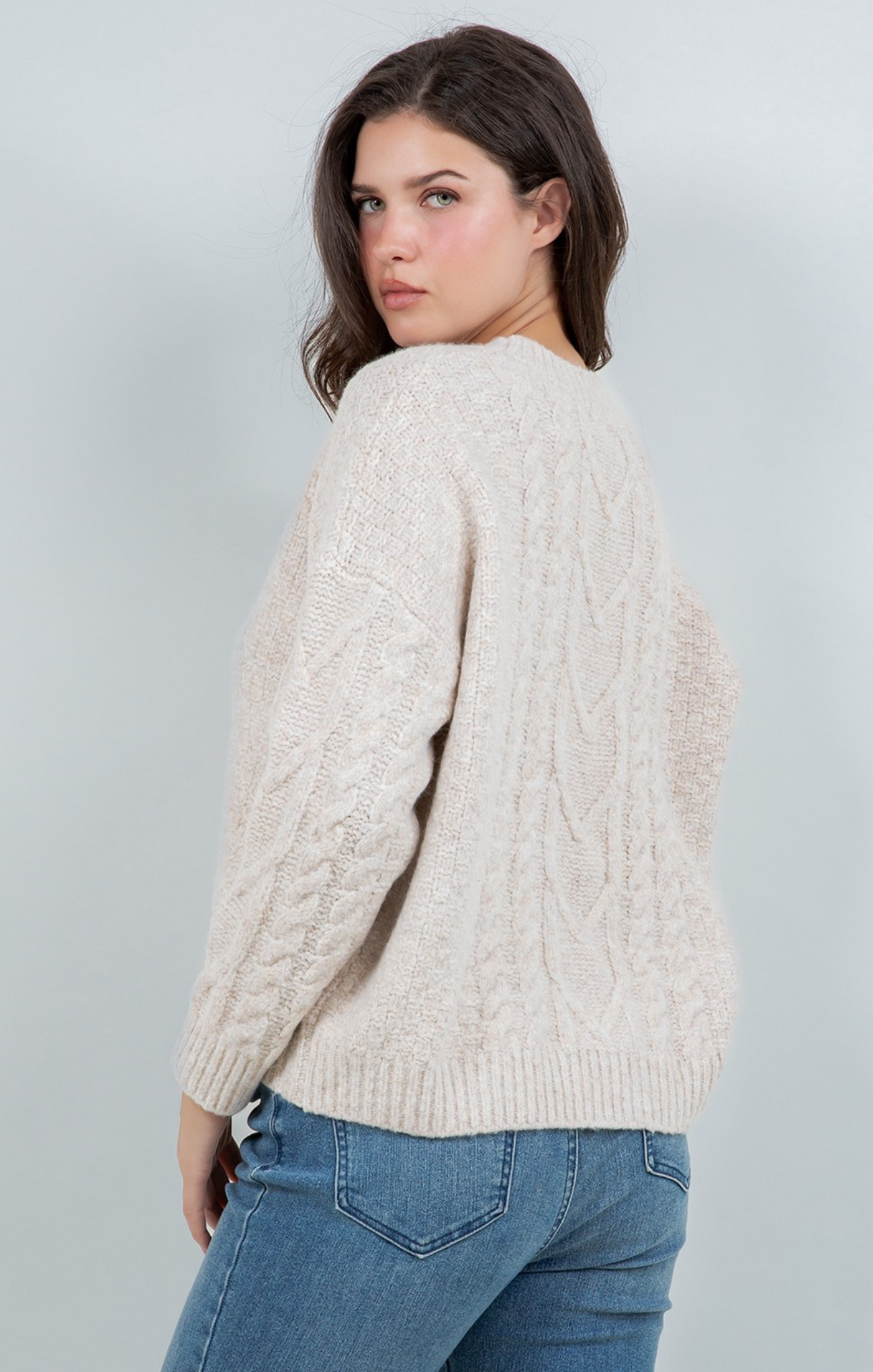 Woman wearing a cream sweater and blue jeans against a plain background