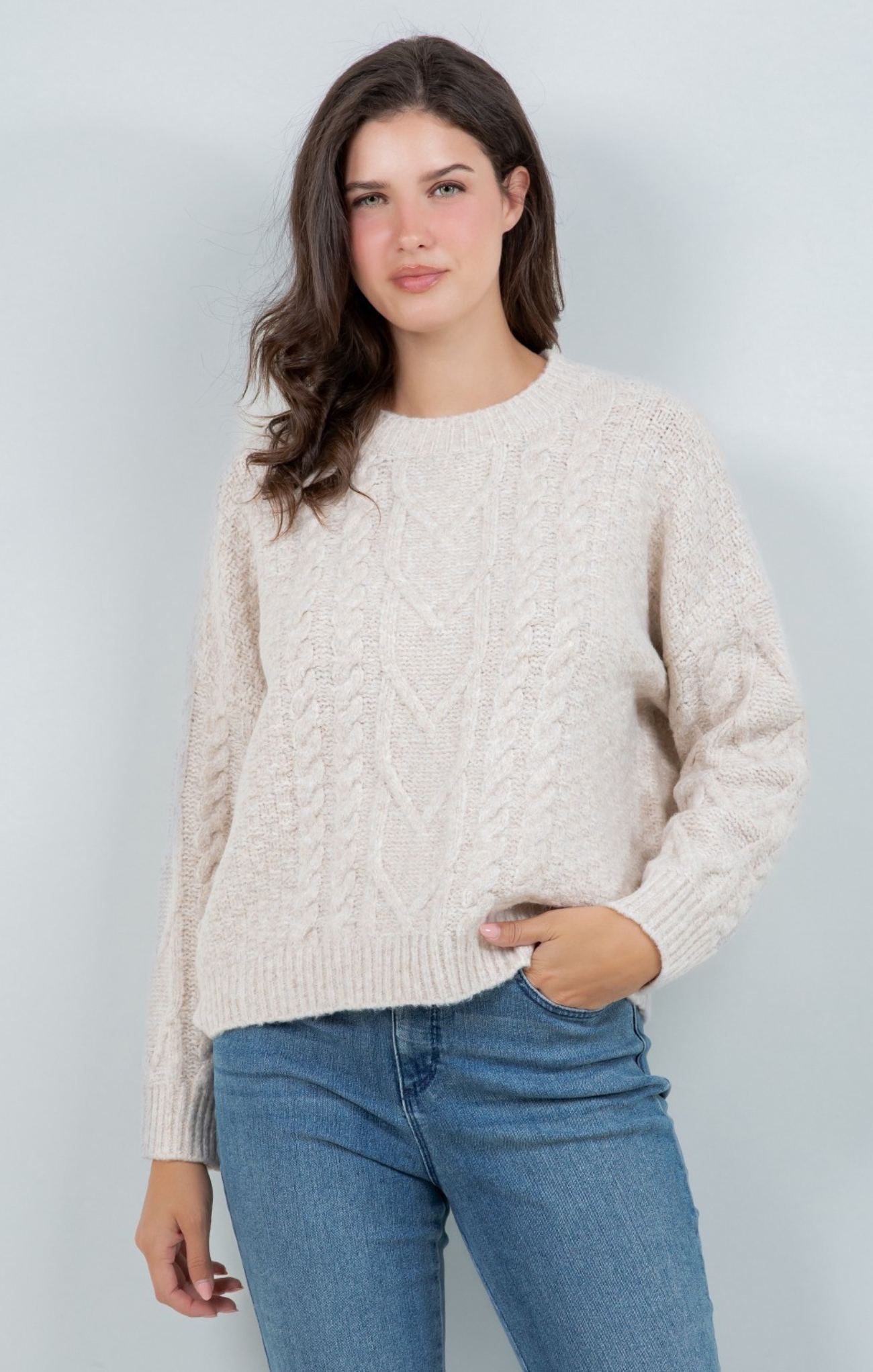 Woman wearing a beige sweater and blue jeans against a light gray background