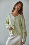 Woman wearing a light green cardigan with brown buttons against a plain background