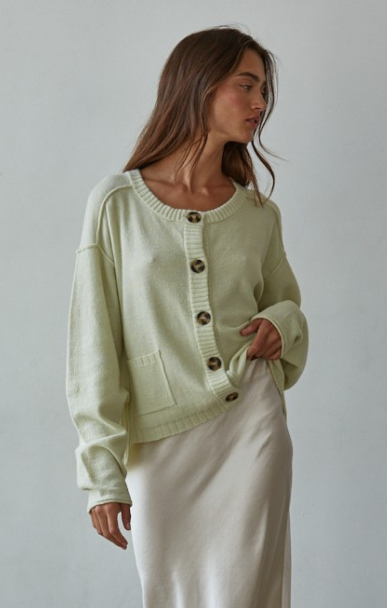 Woman wearing a light green cardigan with button details against a plain background