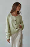 Woman wearing a light green cardigan with button details against a plain background