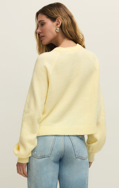 Woman wearing a light yellow sweater and blue jeans against a plain background