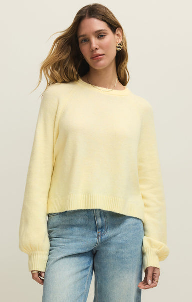 Woman wearing a light yellow sweater and blue jeans against a plain background