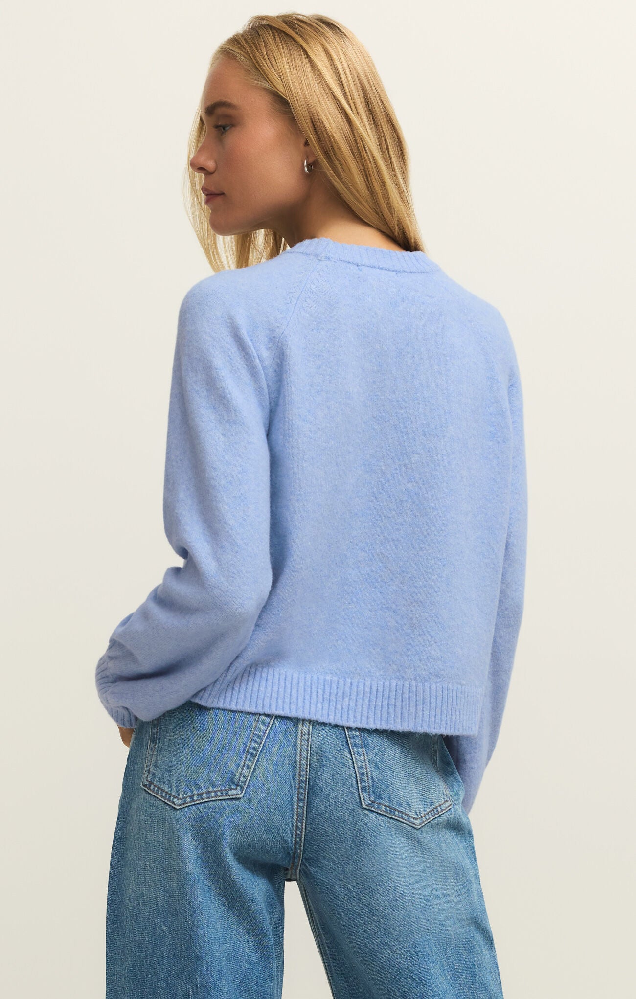 Person wearing a light blue sweater and jeans on a plain background
