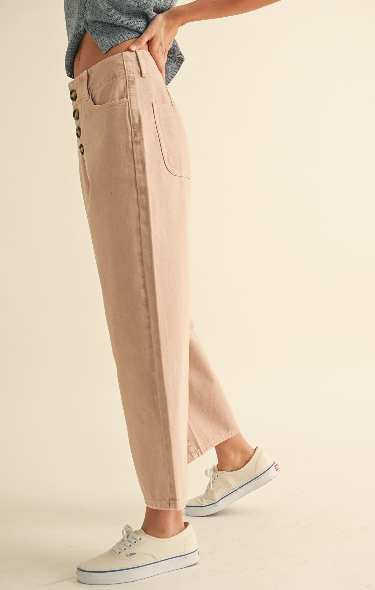 Person wearing beige pants with button details on a plain background