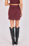 Person wearing a maroon knit skirt and black knee-high boots on a white background