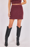 Person wearing a maroon knit outfit with a skirt and black cowboy boots on a white background