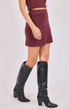 Person wearing a maroon outfit with a skirt and black knee-high boots on a white background