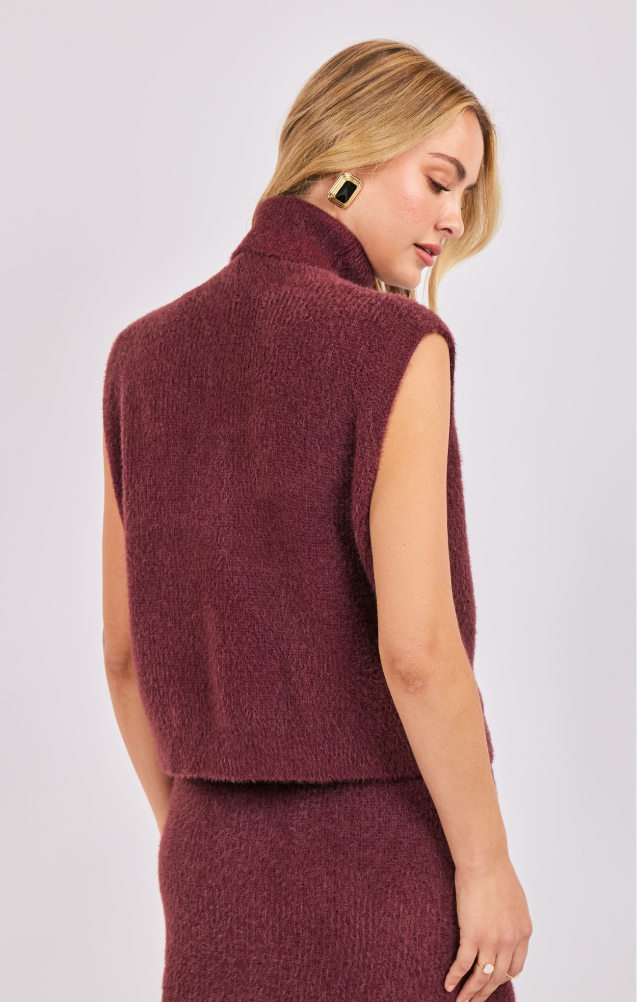 Woman wearing a burgundy sleeveless sweater over a dress on a white background