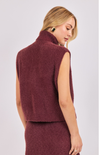 Woman wearing a burgundy sleeveless sweater over a dress on a white background