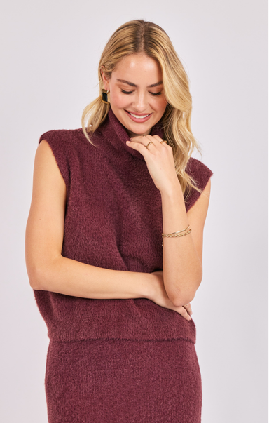 Woman wearing a burgundy sleeveless sweater dress against a plain background