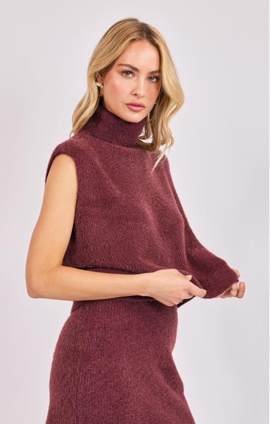 Woman wearing a burgundy sleeveless sweater against a light background