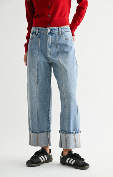 Back view of a model wearing light wash cuffed barrel-leg jeans with a high waist and wide rolled hems, paired with black and white sneakers and a red top.