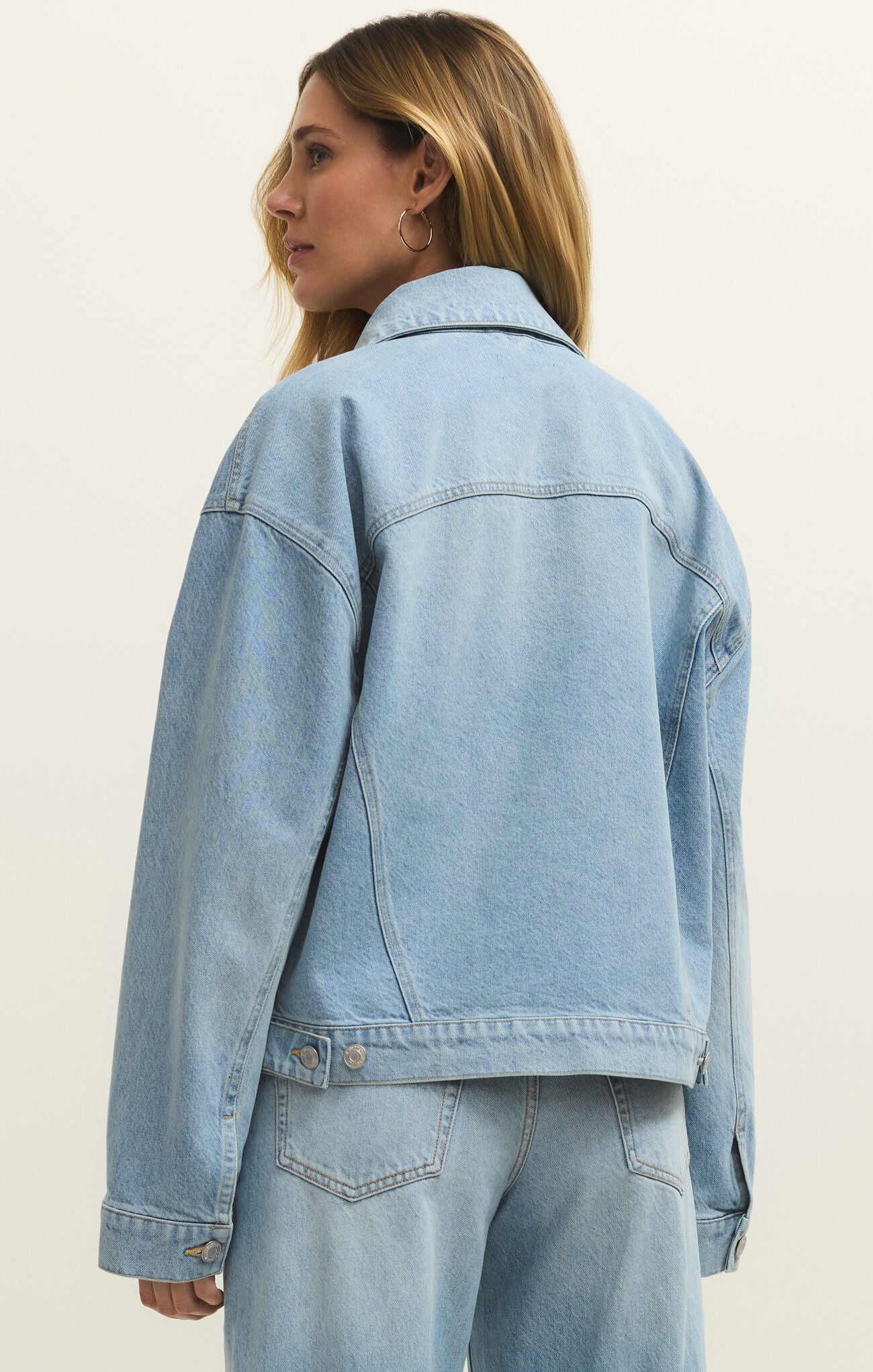 Person wearing a light blue denim jacket on a plain background