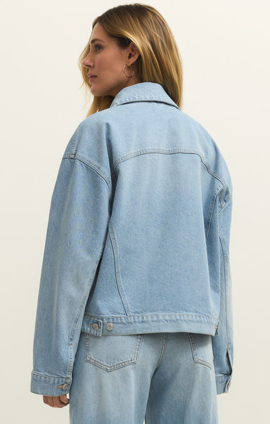 Person wearing a light blue denim jacket on a plain background