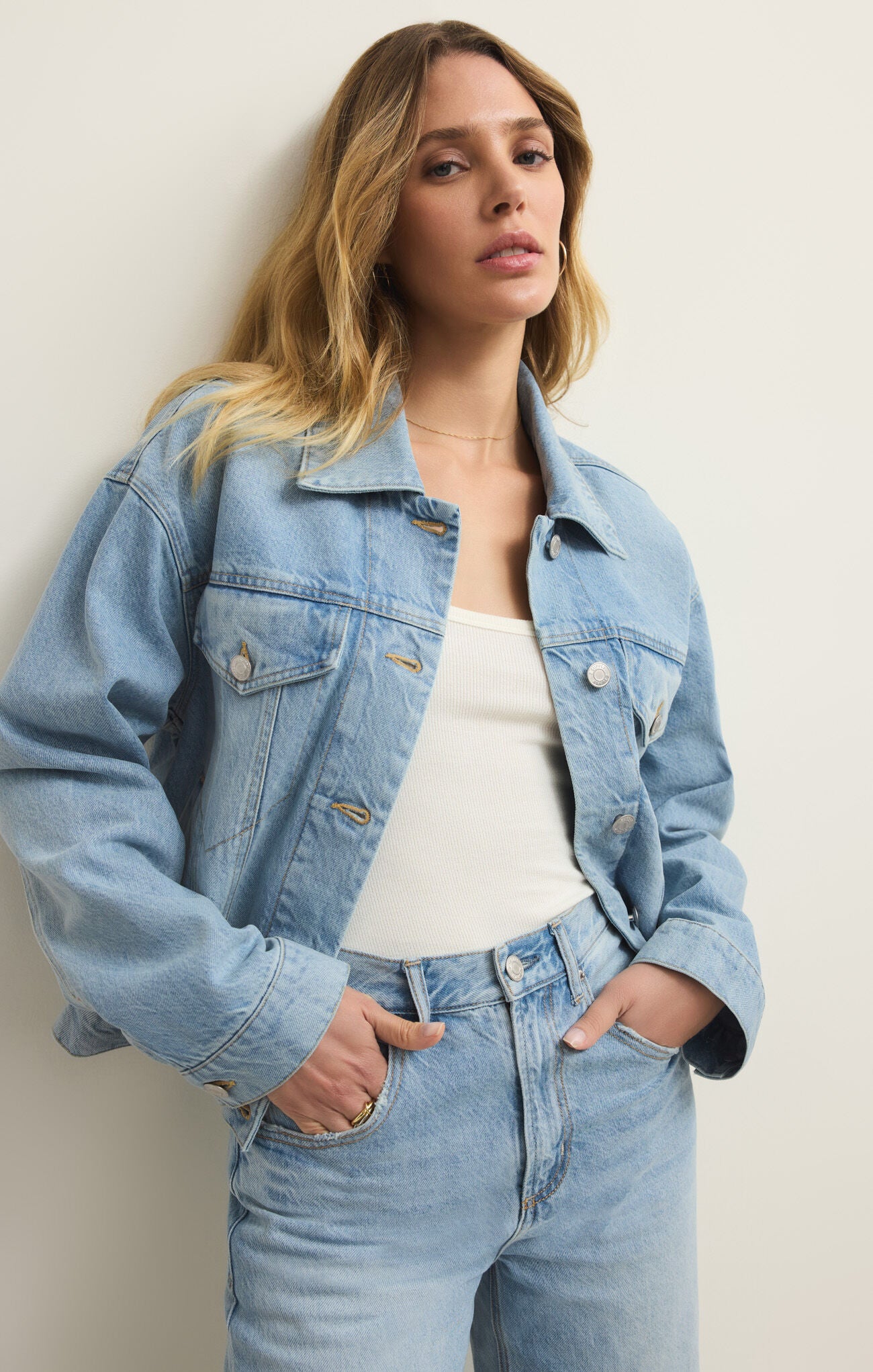 Woman wearing a light blue denim jacket and jeans against a plain background