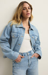 Woman wearing a light blue denim jacket and jeans against a plain background