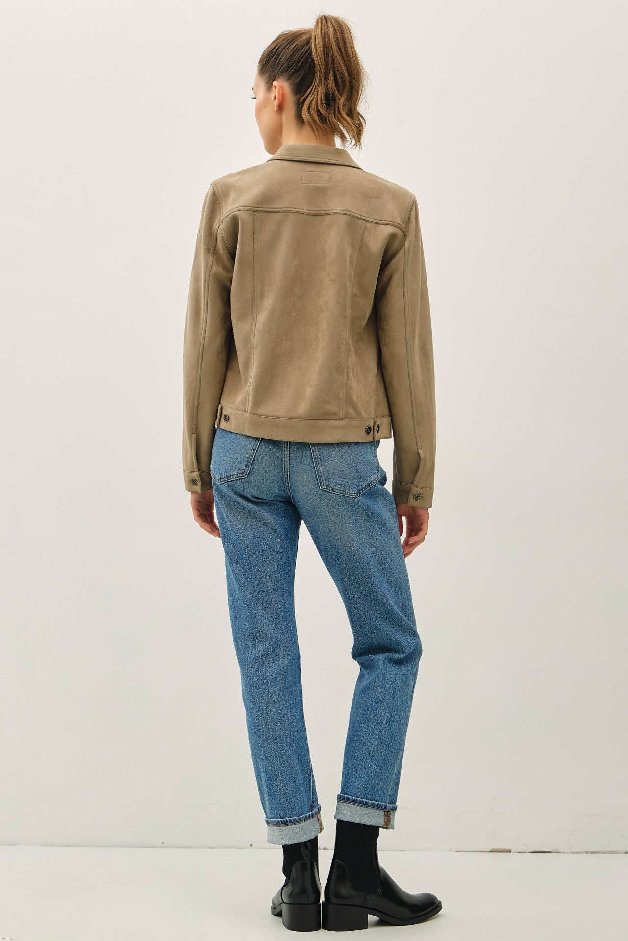 Person wearing a beige jacket and blue jeans on a white background