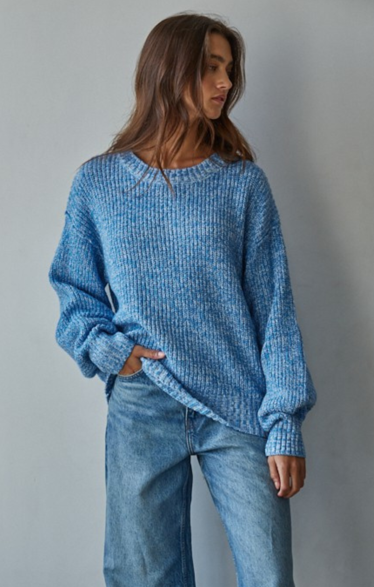 Person wearing a blue knitted sweater and jeans against a gray background