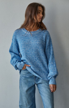 Person wearing a blue knitted sweater and jeans against a gray background
