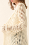 Close-up of a person wearing a beige crochet cardigan on a plain background