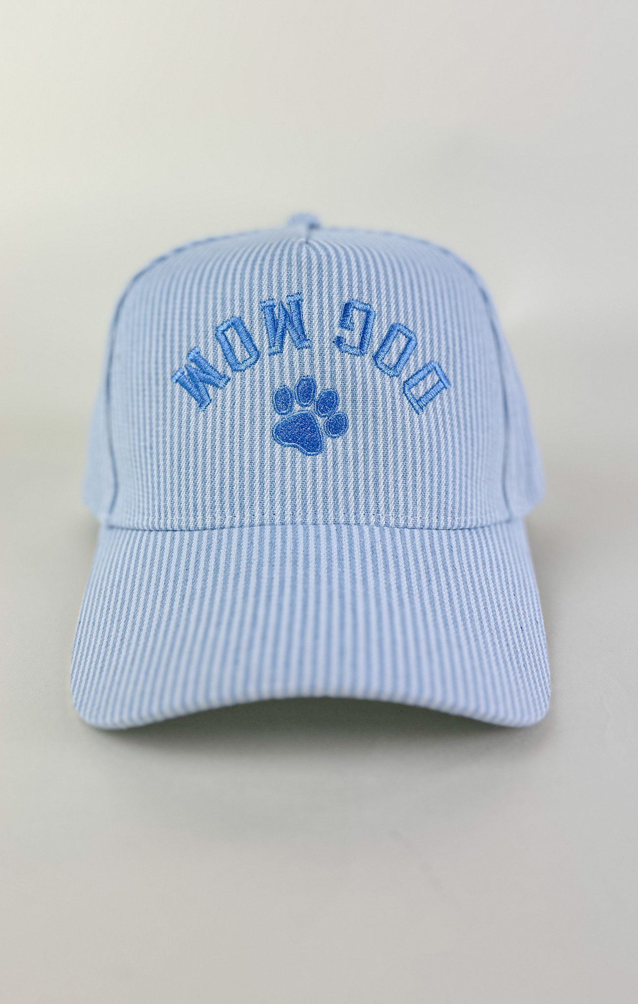 Light blue and white striped baseball cap with “Dog Mom” embroidered in blue lettering above a blue paw print on the front.