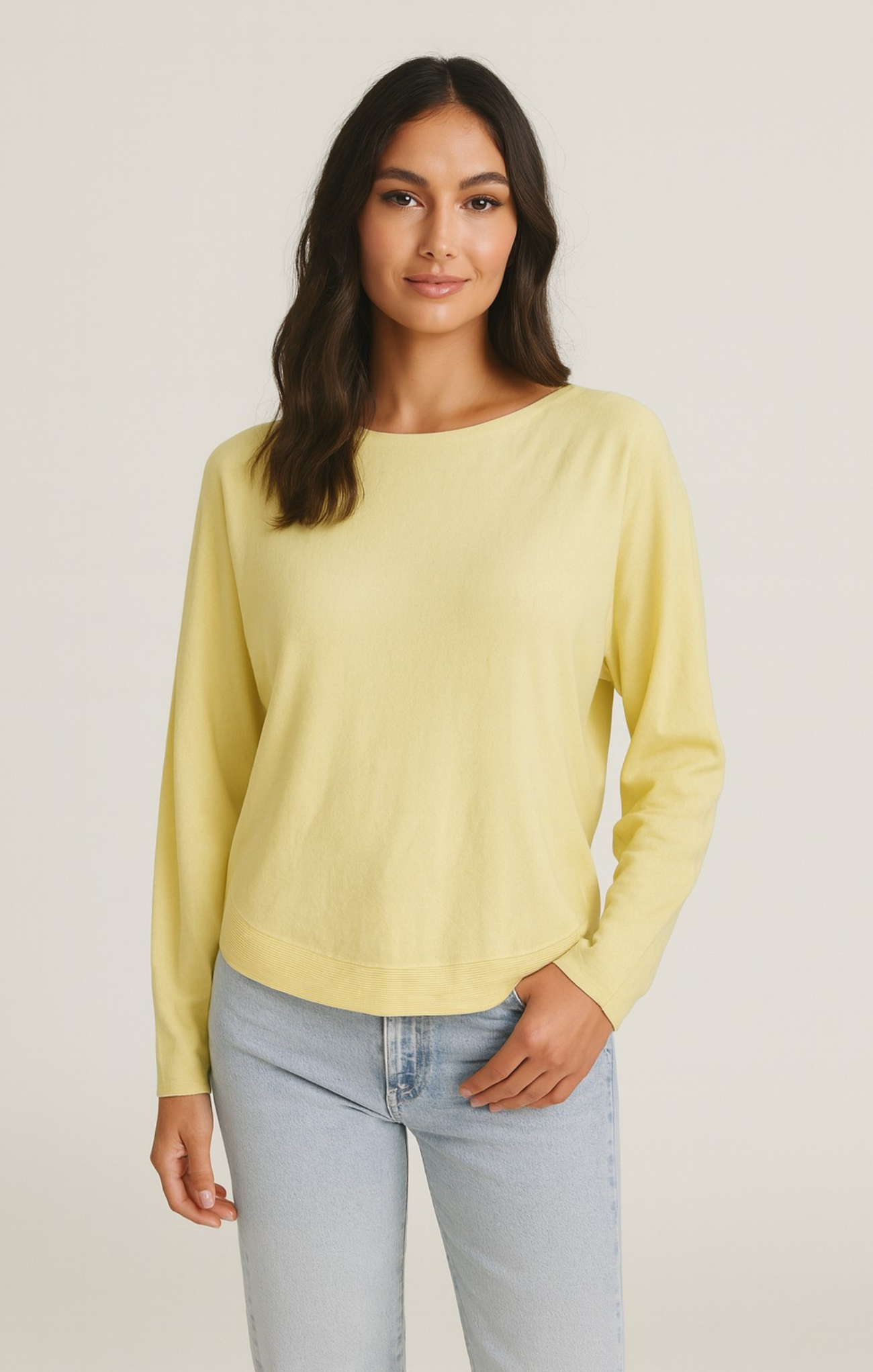 Woman wearing a light yellow sweater and light blue jeans on a plain background