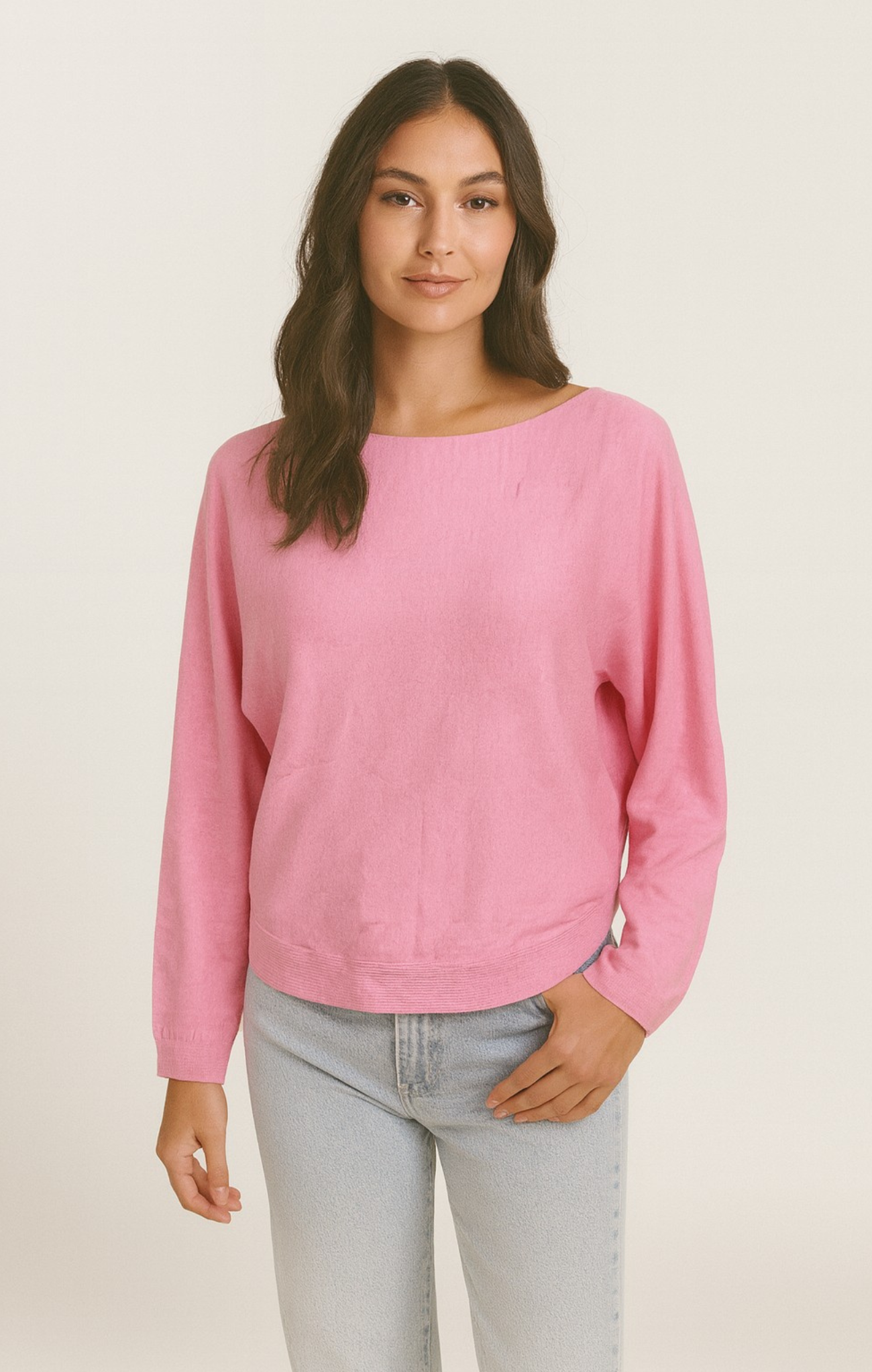 Woman wearing a pink sweater and light gray pants on a beige background