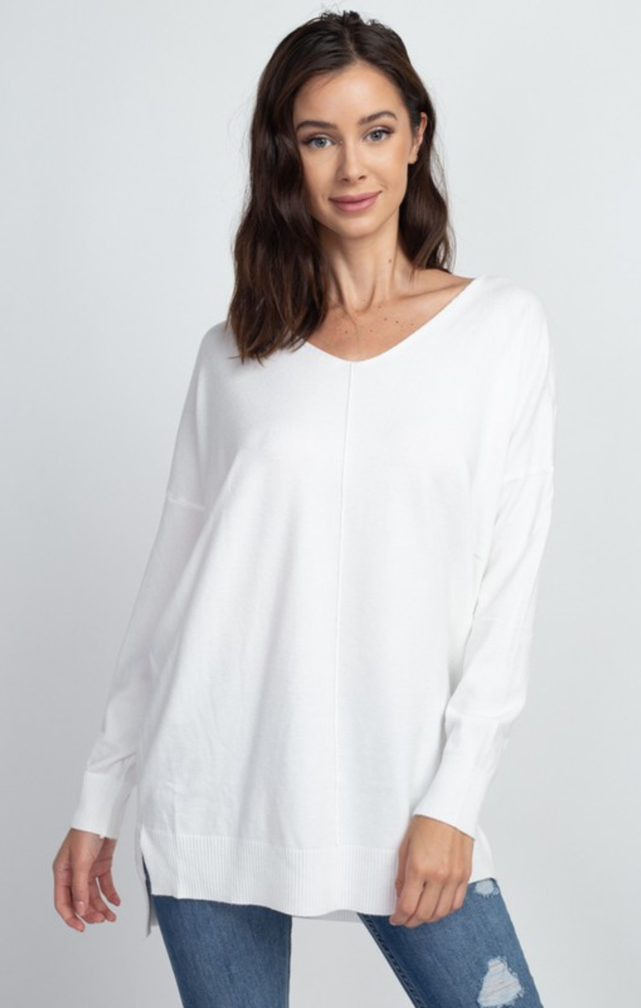 Woman wearing a white long-sleeve top and blue jeans on a light gray background