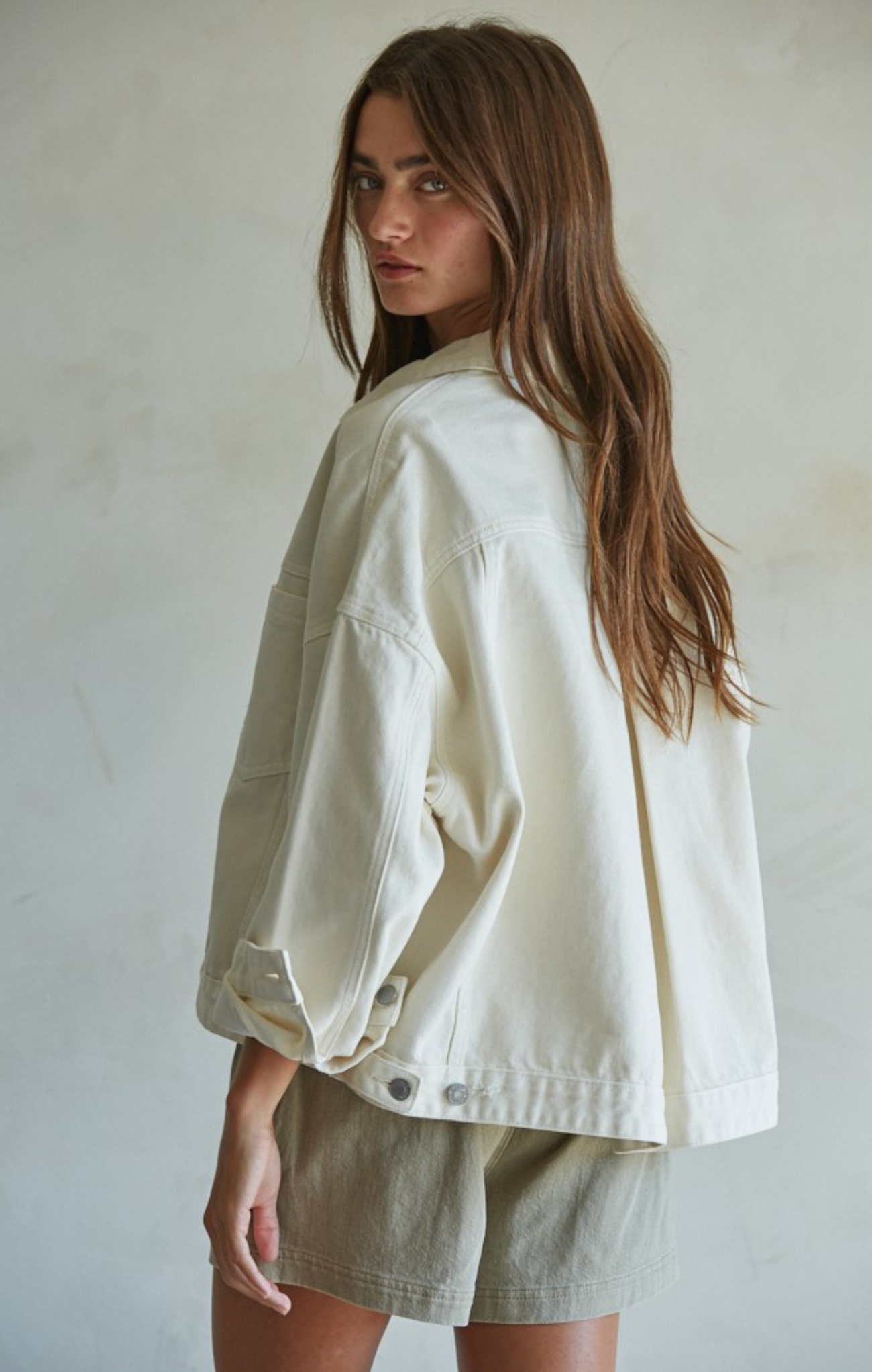 Woman wearing a white jacket and light-colored shorts against a plain background
