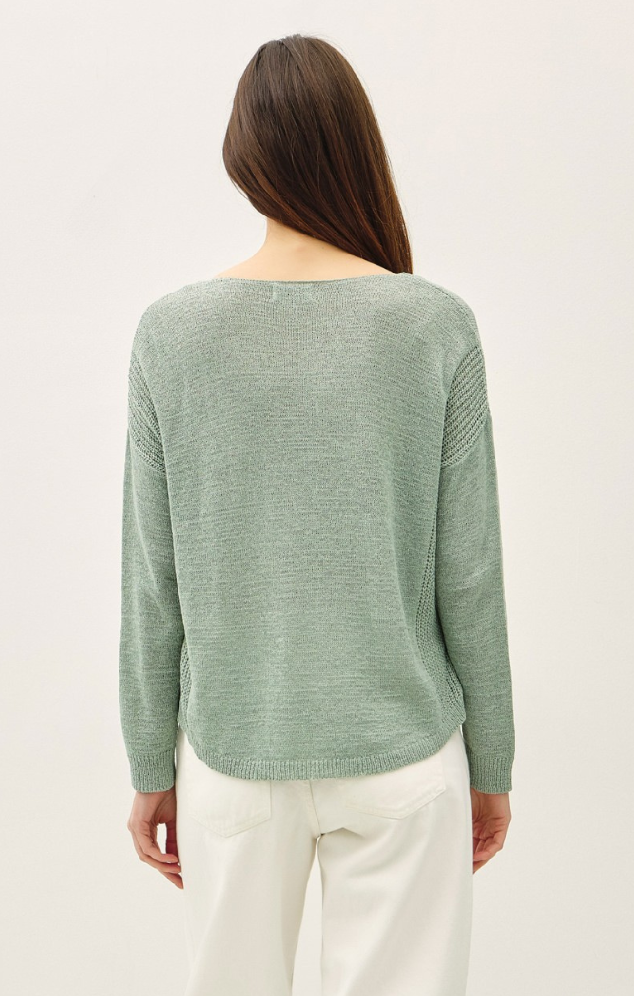 Woman wearing a green sweater and white pants on a light background