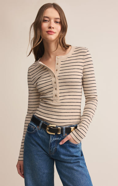 Woman wearing a striped long-sleeve top and blue jeans on a beige background