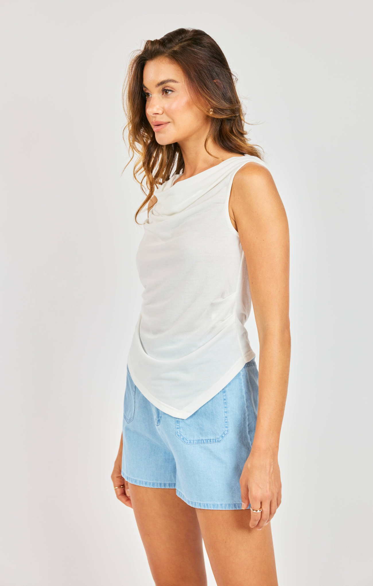 woman wearing white cowl neck tank with blue shorts on white background