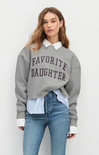 Woman wearing a gray 'Favorite Daughter' sweatshirt with a white collar, blue jeans, and a striped shirt underneath.