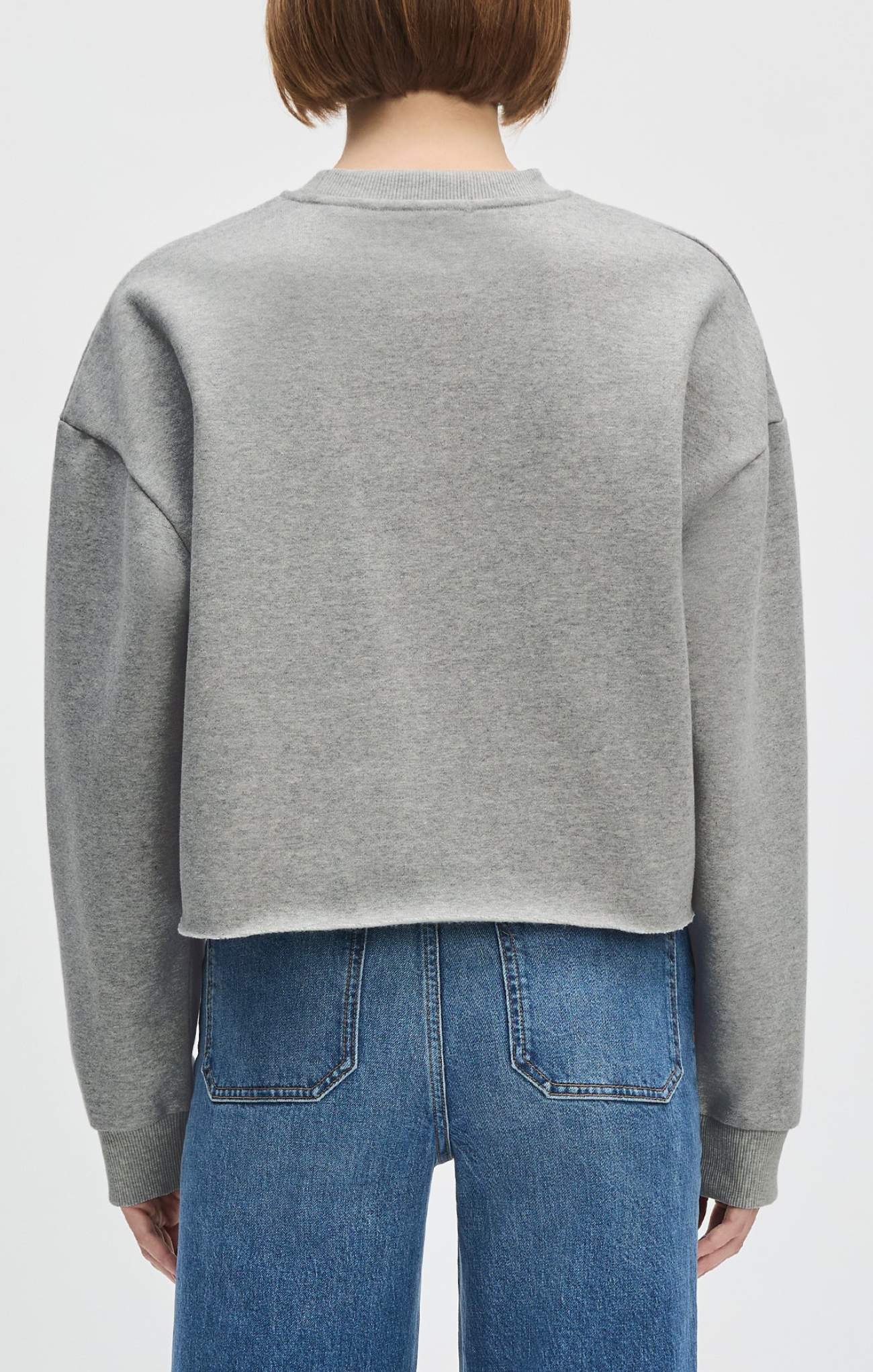 Person wearing a gray sweatshirt and blue jeans on a white background
