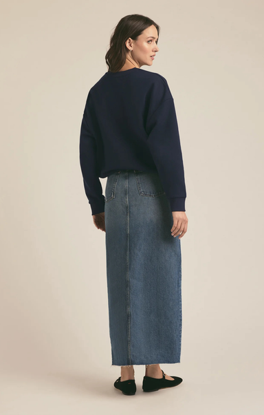 Woman wearing a navy sweater and blue denim skirt on a beige background