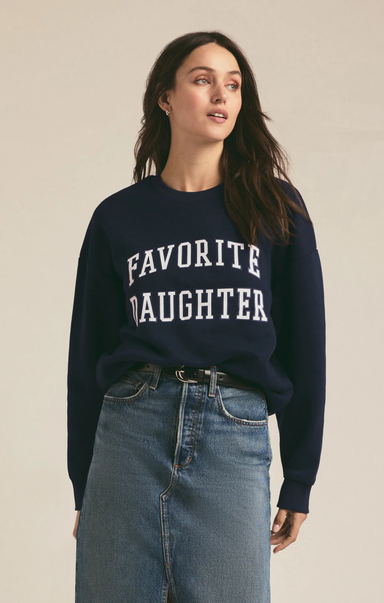 Woman wearing a navy sweater with 'FAVORITE DAUGHTER' text on a beige background