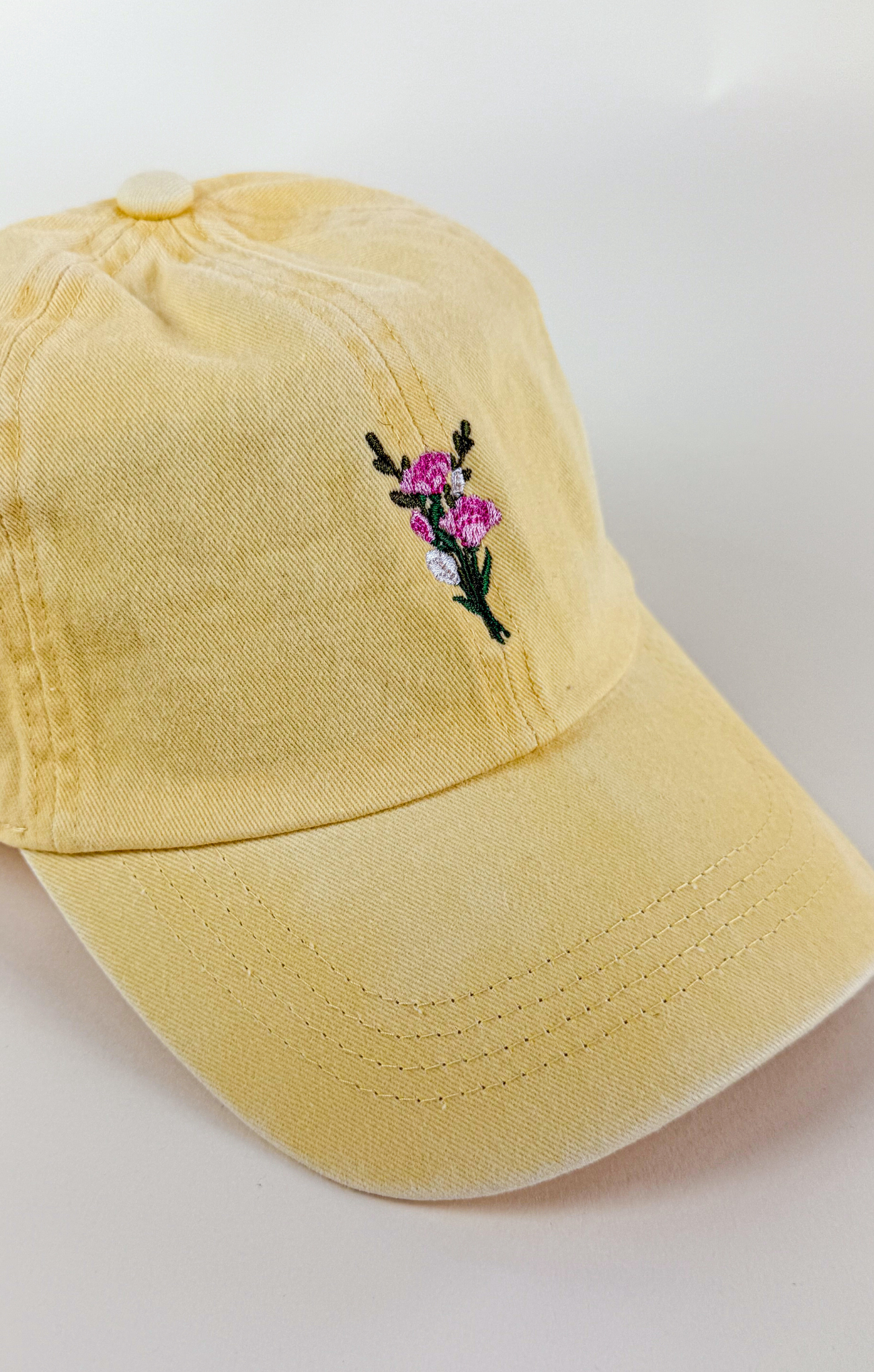 Butter yellow baseball cap with a small embroidered pink and purple flower bouquet centered on the front.