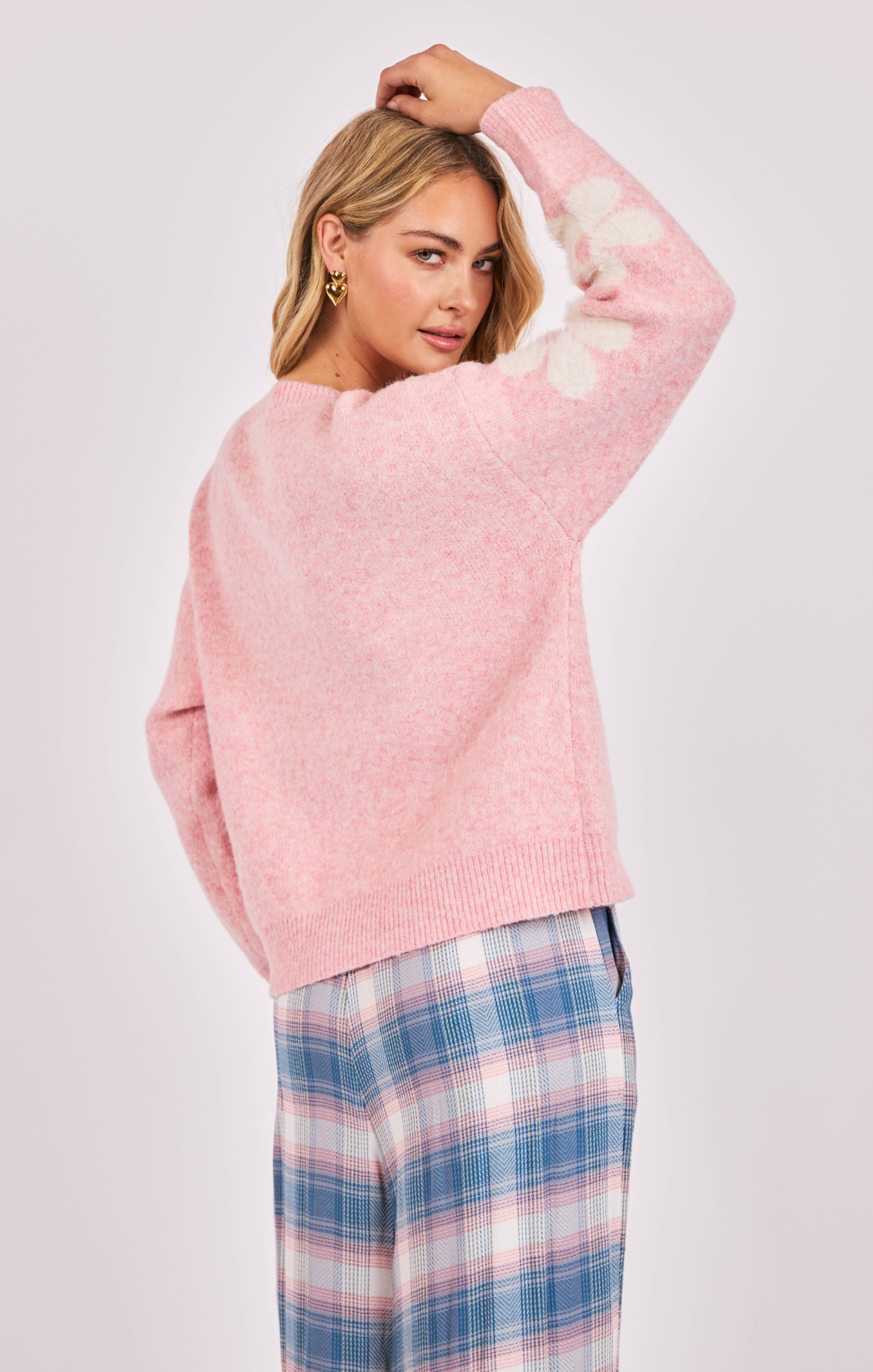 Woman wearing a pink sweater and plaid pants on a light gray background