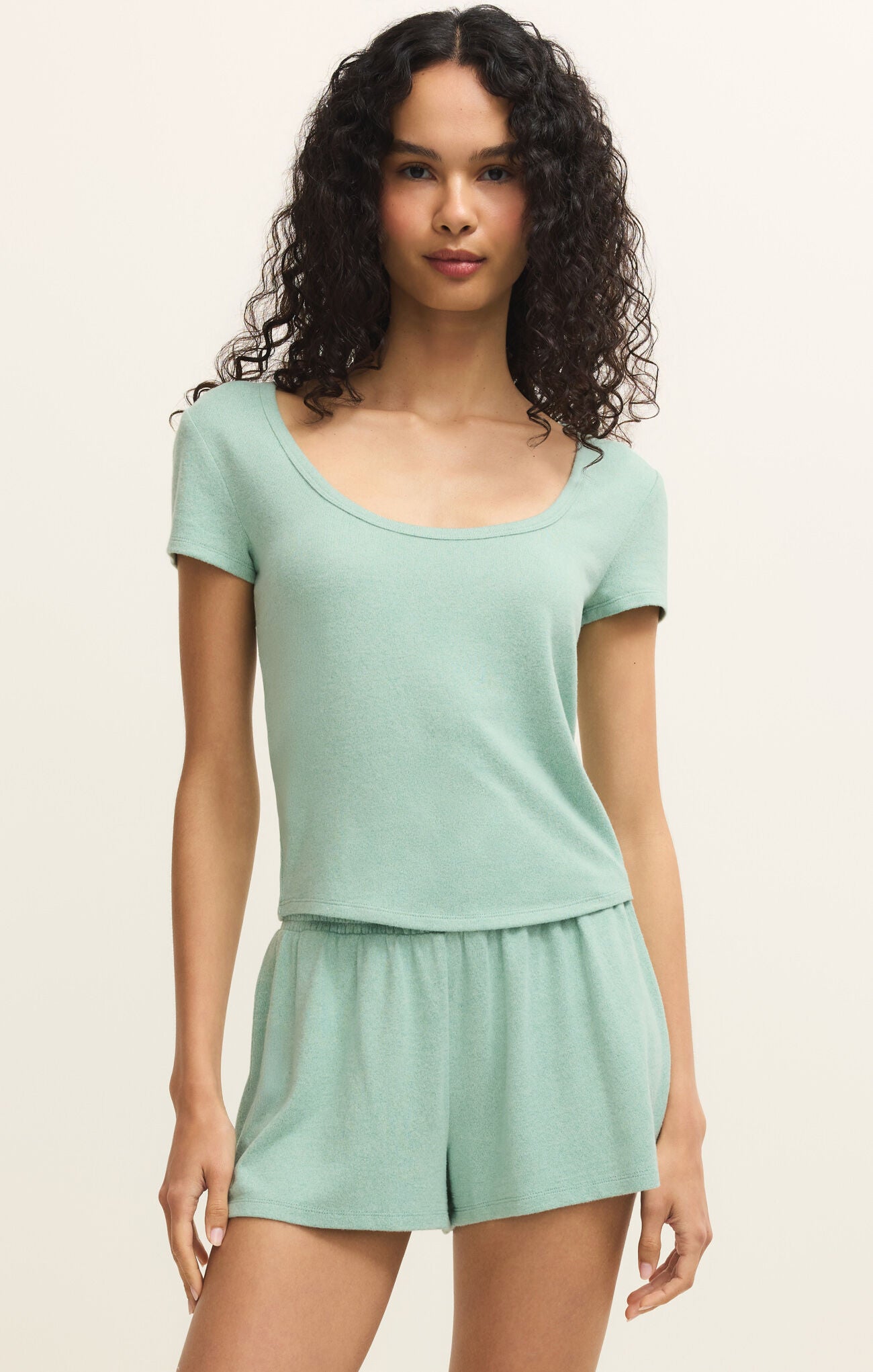 Woman wearing a light green top and shorts set on a beige background