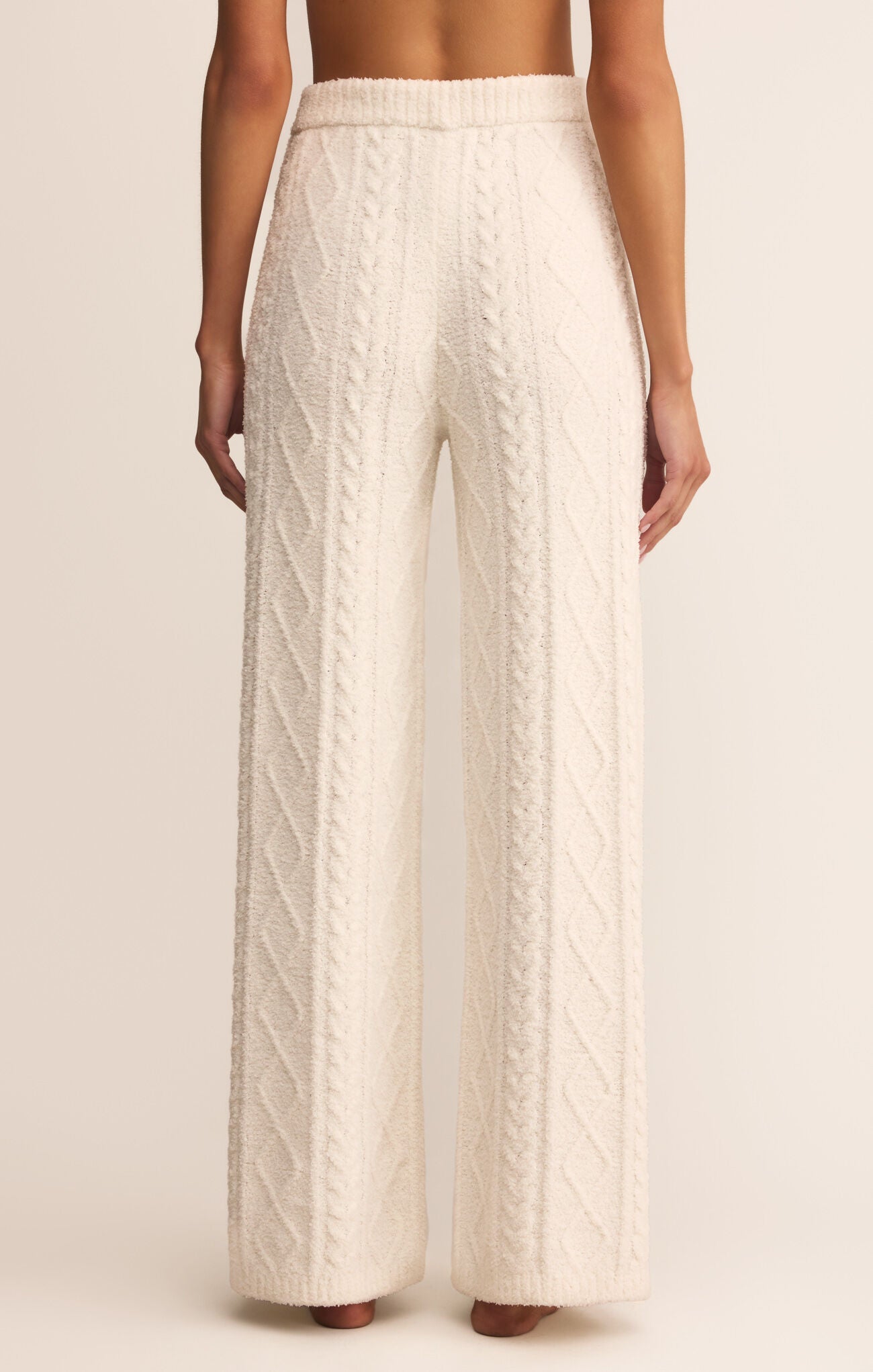White cable knit pants worn by a person on a beige background