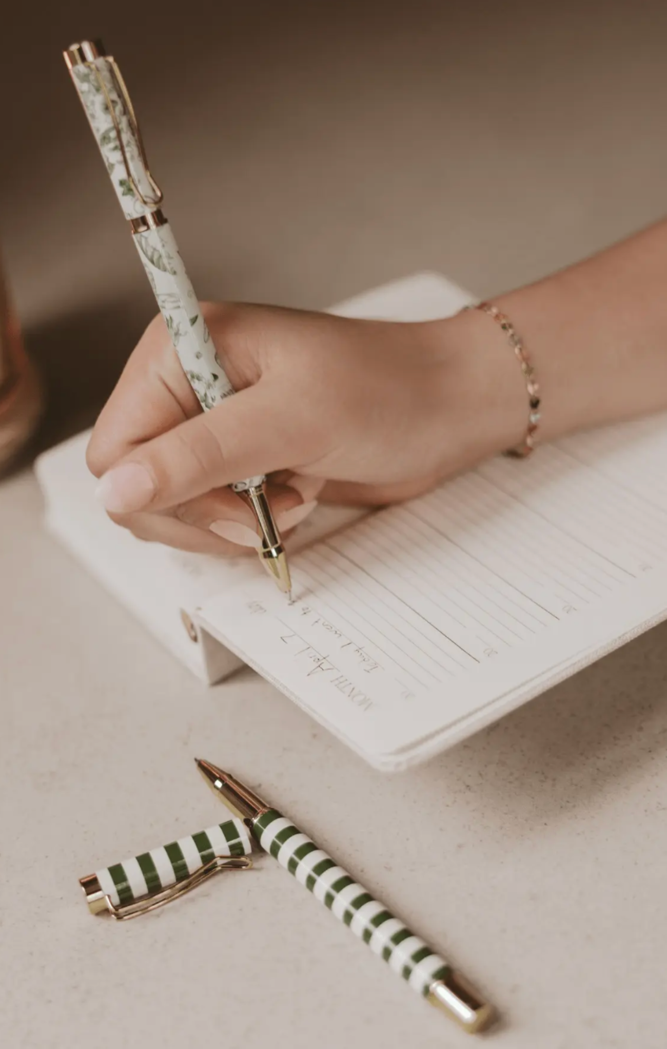 women writing in journal with green floral pen 