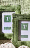 Two green wicker picture frames with a brand label on a textured surface.