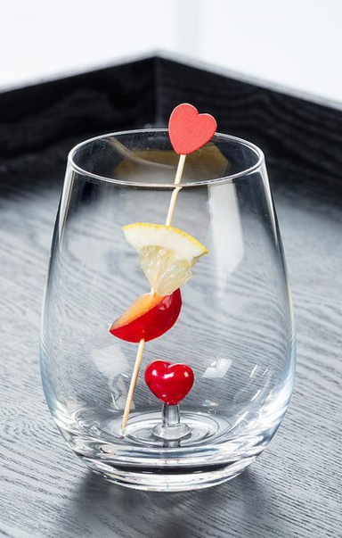 clear glass with heart in the middle with lemon and cherry on stick poking out on grey surface