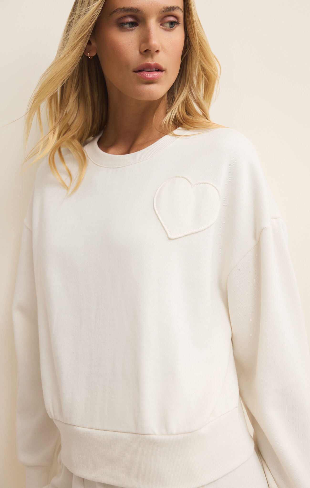 Woman wearing a white sweatshirt with a heart design on a plain background