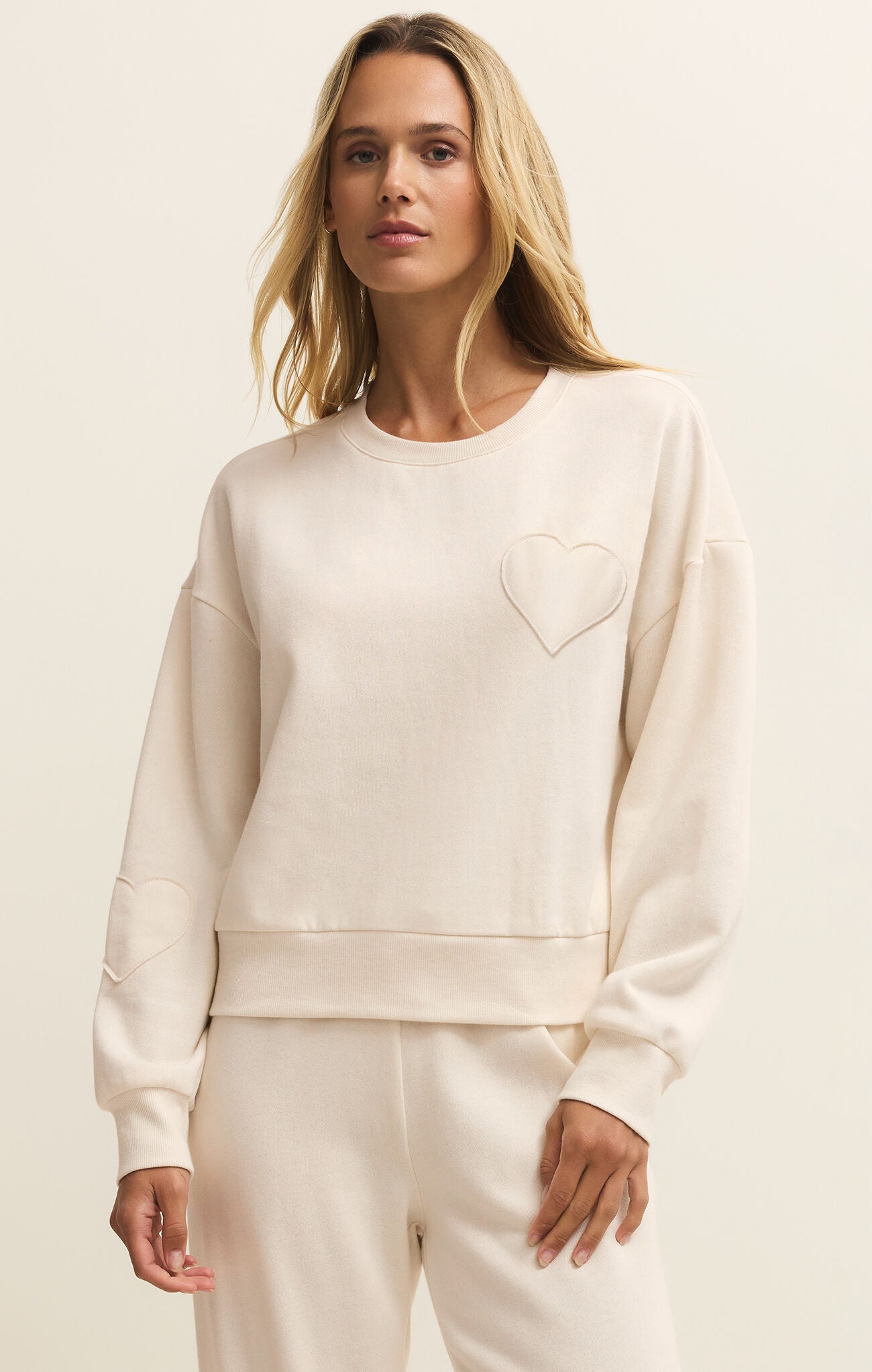 Woman wearing a cream-colored sweatshirt with a heart design on a beige background