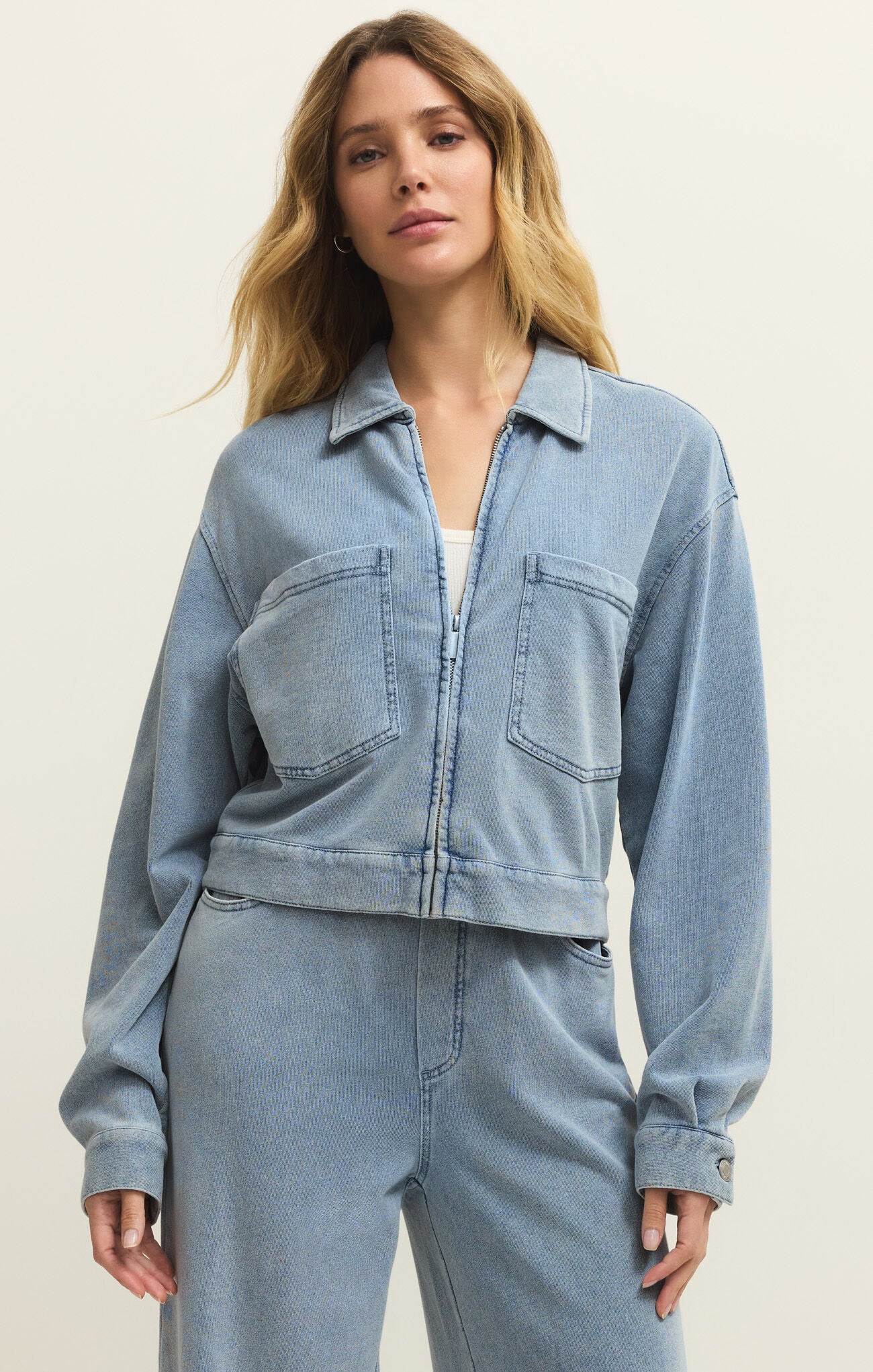 Woman wearing a light blue denim jacket and pants on a plain background