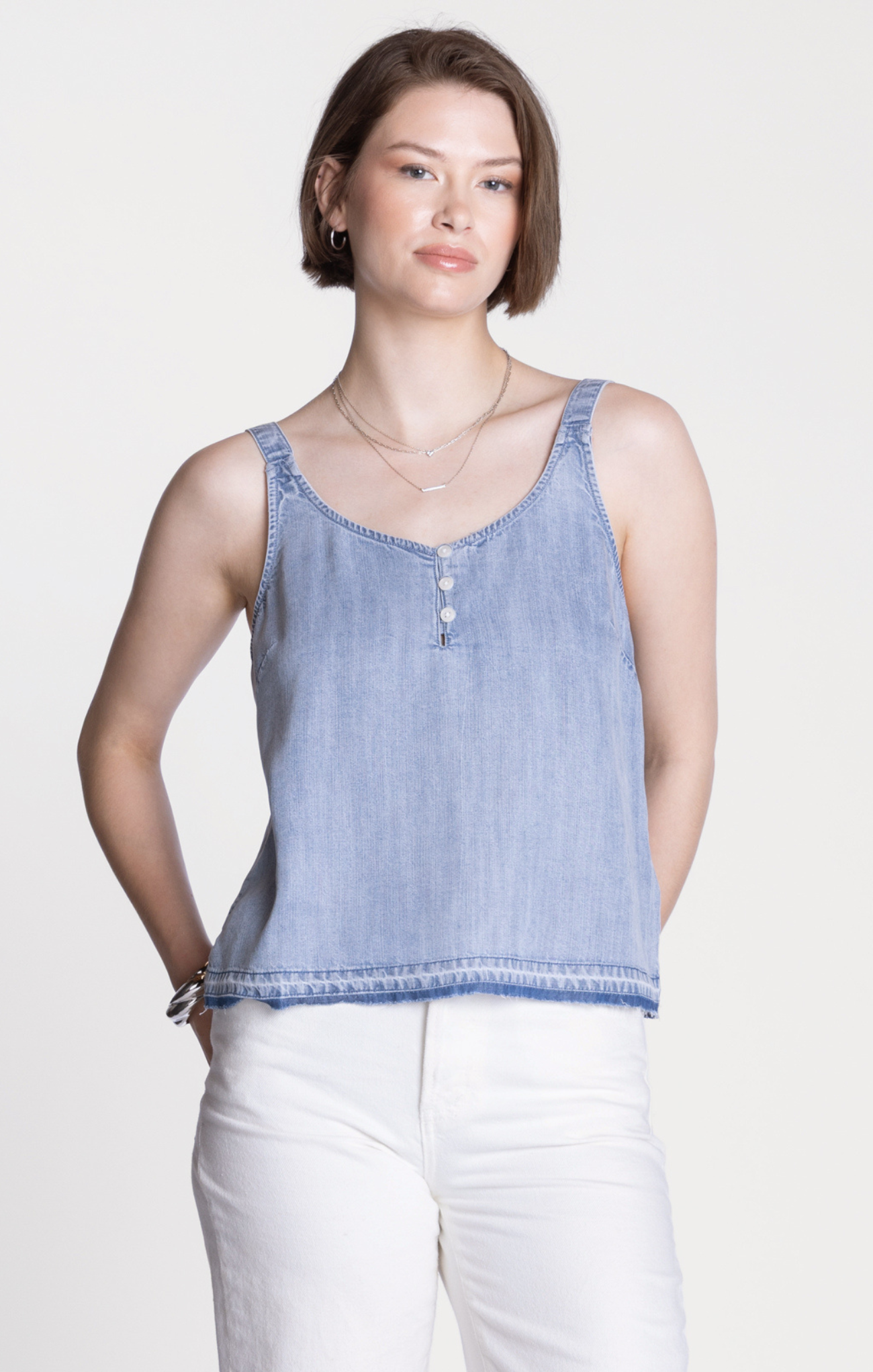 Woman wearing a blue striped tank top and white pants on a light background